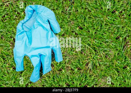 Der blaue gebrauchte medizinische Handschuh liegt auf der linken Seite auf dem grünen Gras. Konzept des Schutzes einer Person vor Coronavirus. Schutz der Ärzte gegen die vi Stockfoto