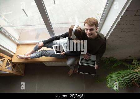 Attraktives junges Paar mit Geräten zusammen, Tablet, Laptop, Smartphone, Kopfhörer drahtlos. Kommunikation, Gadgets Konzept. Technologien, die Menschen in der Selbstisolierung verbinden. Lifestyle zu Hause. Stockfoto