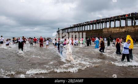 Männer und Frauen in ausgefallenen Kleidern trotzen dem kalten Wasser der Nordsee, während sie an der traditionellen Whitby Lions Boxing Day Dip teilnehmen, um Geld für zu sammeln Stockfoto