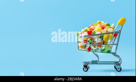 Gefrorenes Gemüse in Spielzeug-Warenkorb auf blauem Hintergrund sortiert. Voll von verschiedenen gefrorenen Gemüse Lebensmittel-Shop Trolley. Banner mit left. Kopierbereich Stockfoto