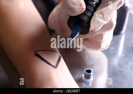 Tätowierer zeichnet Dreieck auf dem Arm der Frau, nah oben Stockfoto