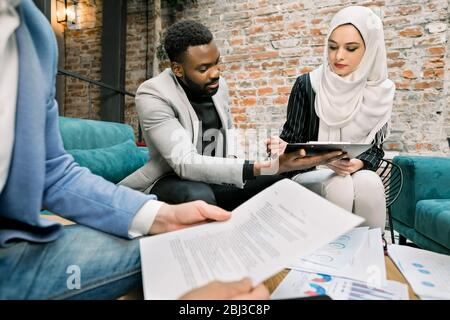 Geschäftskonzept der Unterzeichnung des gemeinsamen Vertrags. Schöne muslimische Geschäftsfrau in weißen Hijab sitzt zusammen mit ihrem bärtigen afrikanischen Geschäft Stockfoto