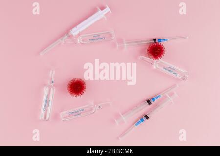 Abstraktes Modell der Coronavirus-Infektion des Coronavirus Stammes. Rotes Virus, Spritze und Ampullen mit Medikamenten auf pinkfarbenem Hintergrund. Auf Ampullen die blaue Aufschrift Coronavirus Impfstoff. Stockfoto