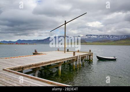 Blick über den Fjord mit einem hölzernen Steg, Fischerboot und schönen Bergen & Inseln im Hintergrund, Eskifjordur, Ost-Island. Stockfoto