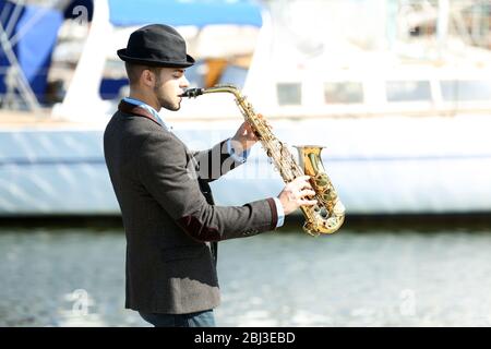 Junger Mann, der am Flussufer auf Saxophon spielt Stockfoto