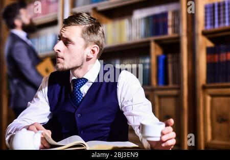 Aristokraten und Elite Konzept. Junge Männer mit antiken Bücherregalen auf Hintergrund. Gebildete Elite oder Aristokraten verbringen Freizeit in der Bibliothek. Intelligent, Mann im Anzug mit guten Manieren halten Tasse Tee. Stockfoto