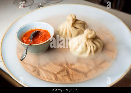 Saftiges Khinkali auf einem weißen Teller. Serviert mit Sauce. Traditionelles Gericht. Auf der Platte befindet sich Holzserviertablett Inculami, die Wasser gegossen hat, das ansteigt. Stockfoto