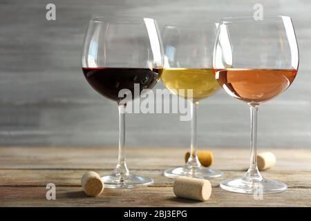 Weingläser in Reihe und Korken auf Holztisch vor grauem Hintergrund Stockfoto