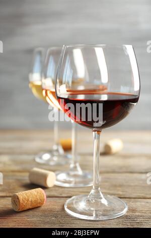 Weingläser in Reihe und Korken auf Holztisch vor grauem Hintergrund Stockfoto