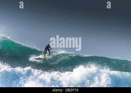 Ein Surfer, der auf dem Kamm einer riesigen, hoch aufragenden Welle in Fistral in Newquay in Cornwall reitet. Stockfoto