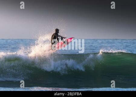 Spektakuläre Surfaktion, während ein Surfer eine Welle im Abendlicht in Fistral in Newquay in Cornwall reitet. Stockfoto