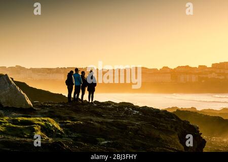 Menschen, die auf Felsen stehen und einen spektakulären Sonnenuntergang am Little Fistral in Newquay in Cornwall beobachten. Stockfoto
