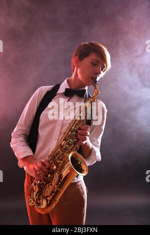 Talentfrau spielt professionell Saxophon in rotem Rauch Stockfoto