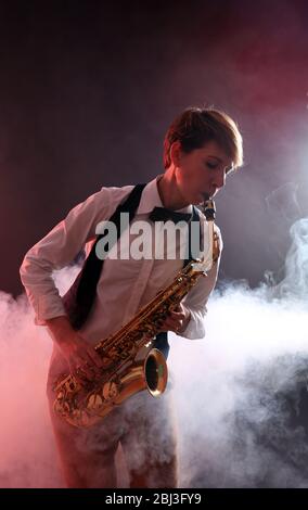 Talentfrau spielt professionell Saxophon in rotem Rauch Stockfoto