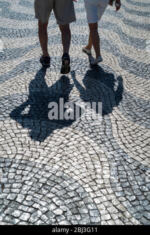 Schatten eines Mannes und einer Frau über Pavierer, die wellenförmige Linien und geometrische Muster auf dem Rossio-Platz in der Stadt Lissabon, Portugal, bilden Stockfoto