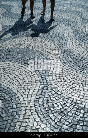 Schatten eines Mannes und einer Frau über Pavierer, die wellenförmige Linien und geometrische Muster auf dem Rossio-Platz in der Stadt Lissabon, Portugal, bilden Stockfoto