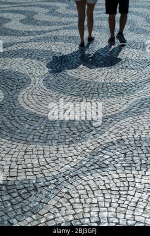 Schatten eines Mannes und einer Frau über Pavierer, die wellenförmige Linien und geometrische Muster auf dem Rossio-Platz in der Stadt Lissabon, Portugal, bilden Stockfoto