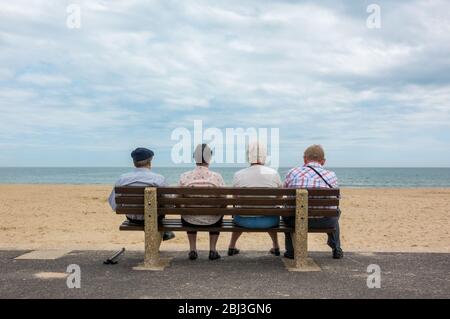Rückansicht von vier anonymen Senioren, alten Paaren, älteren Männern und Frauen, die auf einer Bank am Strand sitzen Stockfoto