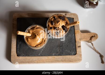 Dalgona Kaffee, ein trendiges Getränk. Zwei Gläser Dalgona Kaffee auf einem Holzbrett Stockfoto