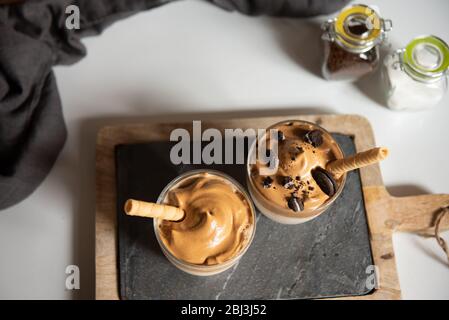 Dalgona Kaffee, ein trendiges Getränk. Zwei Gläser Dalgona Kaffee auf einem Holzbrett Stockfoto