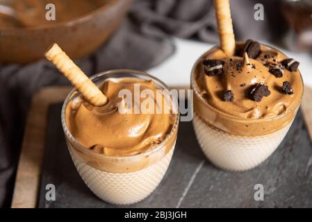 Dalgona Kaffee, ein trendiges Getränk. Zwei Gläser Dalgona Kaffee auf einem Holzbrett Stockfoto