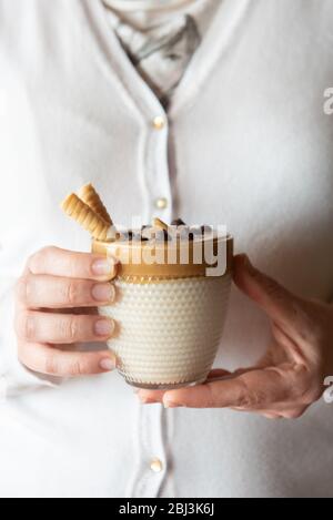 Weibliche Hände halten selbstgemachten Dalgon Kaffee in einem Glas mit Milch auf einem Holzständer. Trendy flauschig cremig Schlagsahne Kaffee. Stockfoto