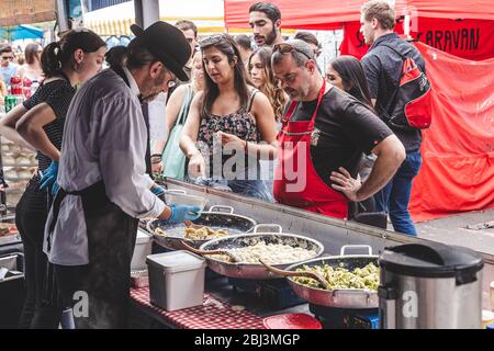 London/UK - 22/07/18: Mann kauft Lebensmittel in einem Stand auf einem Lebensmittelmarkt; Blick von innen; der Verkäufer kocht eine andere Art von Pasta in den Pfannen Stockfoto