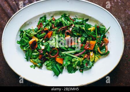 Gesunder veganer Salat aus frischem Gemüse mit Zwiebeln, Gurken, Tomaten, Paprika und Blättern mit Sauce und Olivenöl in einem weißen Teller Stockfoto