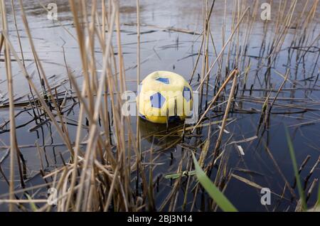 Gelber Fußball gefunden, weggeworfen in Wasser umgeben von Pondweeds, Kent England. Stockfoto