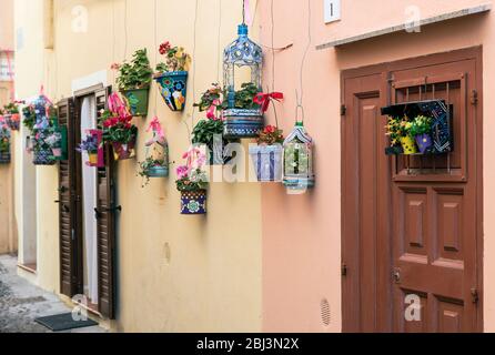 Handbemalte Pflanzgefäße und bunte Blumen schmücken eine charmante Straße in Alghero auf Sardinien. Stockfoto