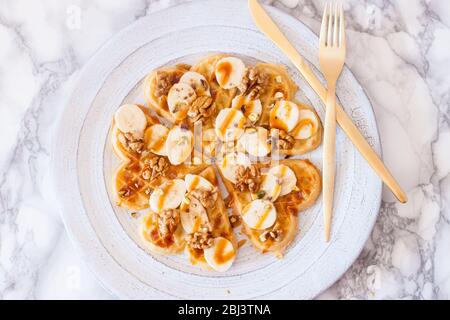 Belgien herzförmige Waffeln mit Bananen, Ahornsirup, gesalzenem Karamell und Nüssen. Draufsicht. Stockfoto