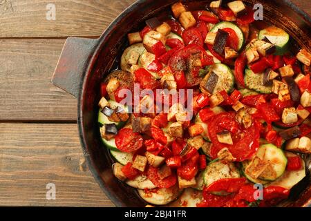 Leckere vegetarische Ratatouille aus Auberginen, Kürbis, Tomaten und Zwiebeln in schwarzer Gusseisenpfanne, auf Holztisch Hintergrund Stockfoto