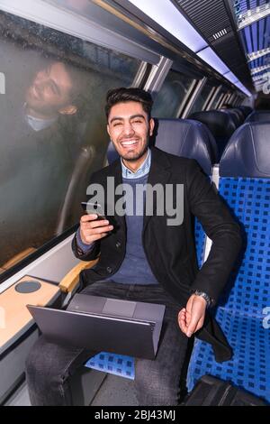 Mann sitzt im Zug mit Notebook und Telefon in der Hand Stockfoto