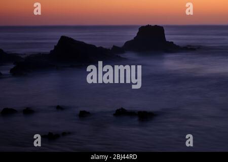 Strand Praia da Zambujeira do Mar bei Sonnenuntergang, Felsen und Wellen in Bewegung. Solo Backpacker Trekking auf der Rota Vicentina und Fischer-Trail in EINEM Stockfoto