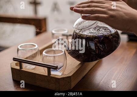 Der violette florale Kräutertee wird vom Brauer in die Tasse gegossen. Stockfoto