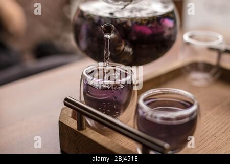 Der violette florale Kräutertee wird vom Brauer in die Tasse gegossen. Stockfoto