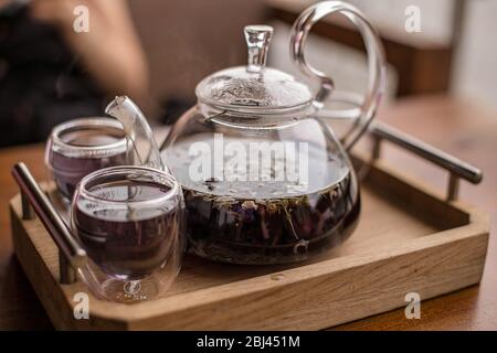 Der violette florale Kräutertee wird vom Brauer in die Tasse gegossen. Stockfoto