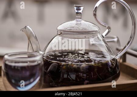 Der violette florale Kräutertee wird vom Brauer in die Tasse gegossen. Stockfoto