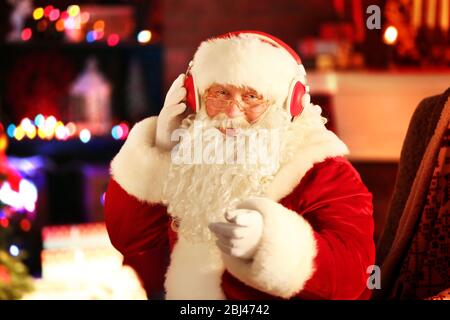 Weihnachtsmann sitzt mit Kopfhörern in bequemen Schaukelstuhl zu Hause sitzen Stockfoto