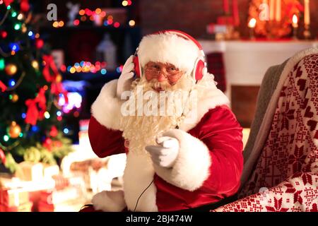 Weihnachtsmann sitzt mit Kopfhörern in bequemen Schaukelstuhl zu Hause sitzen Stockfoto