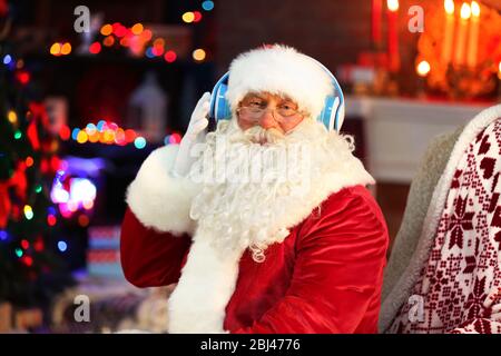 Weihnachtsmann sitzt mit Kopfhörern in bequemen Schaukelstuhl zu Hause sitzen Stockfoto