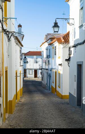 Typische weiße und gelbe Häuser und Laternen in einer engen Kopfsteinpflasterstraße in Evora, Portugal Stockfoto