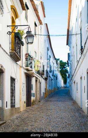 Typische Straßenszene aus weißen und gelben Häusern, Laternen und engen Kopfsteinpflasterstraßen in Evora, Portugal Stockfoto