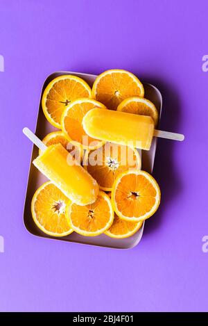 Orange Stielschnäkel Sorbet und Scheiben von Orangen in einem Tablett, Draufsicht auf einem lila Hintergrund. Köstliches hausgemachtes Orangeneis Stockfoto