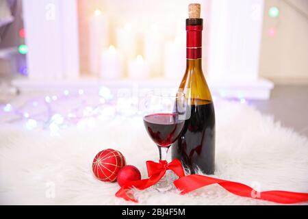 Flasche und Glas Wein mit Weihnachtsdekor vor farbenfrohem Bokeh-Licht Hintergrund Stockfoto