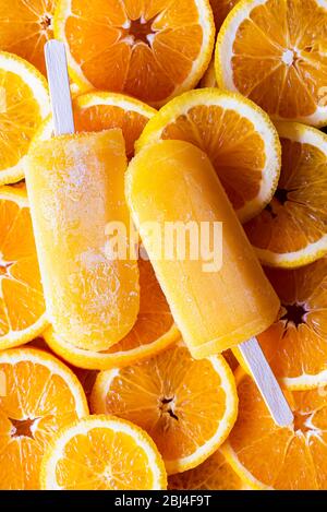 Zwei Orangeneis auf dem Stock und Scheiben frischer Orangen. Fruitty Eis Eis-Eis-Eis-Eis, sommerliche Erfrischung. Sommerdessert Sorbet-Eiszapfen Stockfoto