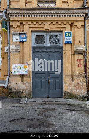 Fassade des Retro-Gebäudes und beschädigte Asphalt Bürgersteig. Gelbe Backsteinmauer des historischen Gebäudes in Kiew Stadt. Alte grau bemalte Holztür mit verzierten f Stockfoto