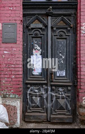 Eingang zu verlassenen historischen Gebäude mit alten Holztür mit verzierten schwarzen Paneelen an roten Ziegelwand. Architektur der europäischen Stadt. Retro-Gebäude e Stockfoto