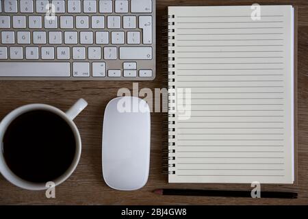 Ein hoher Blickwinkel auf einen Schreibtisch mit Tastatur, Kaffee, Maus und spiralförmigem Notizbuch mit liniertem Kopierraum für Notizen Stockfoto