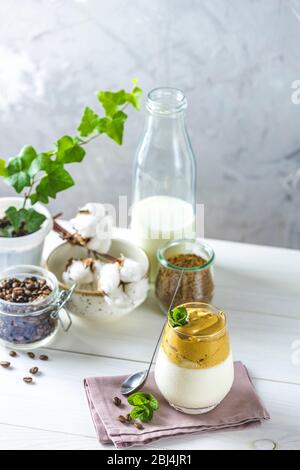 Ein Glas Iced Dalgona Coffee, ein trendiger flauschiger cremiger Schlagkaffee, dekoriert mit Minze und Zutaten auf hellem rustikalem Hintergrund, Kopierraum. Stockfoto